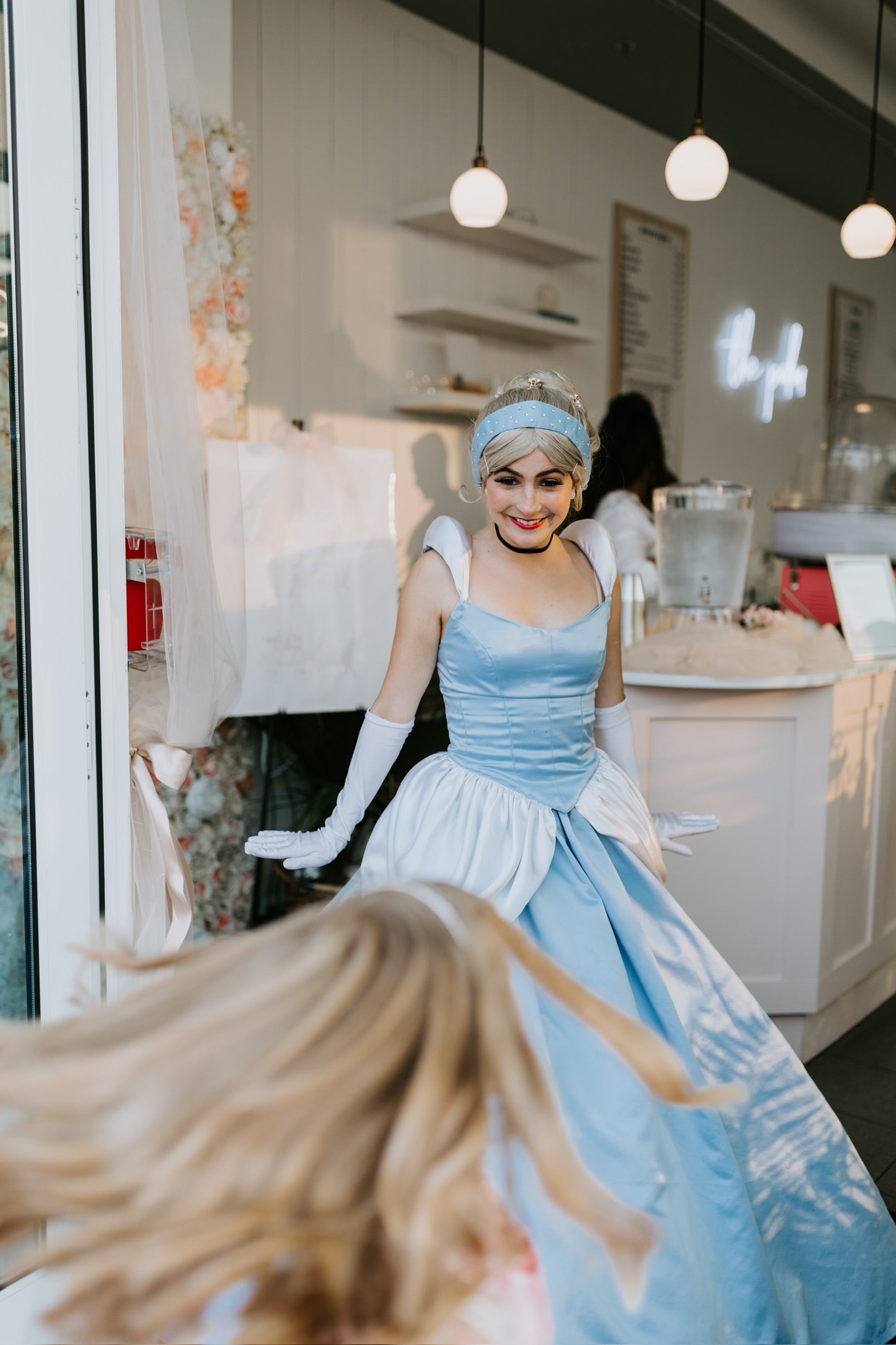 Woman in a blue dress with gloves standing in a room with white walls and hanging lights.